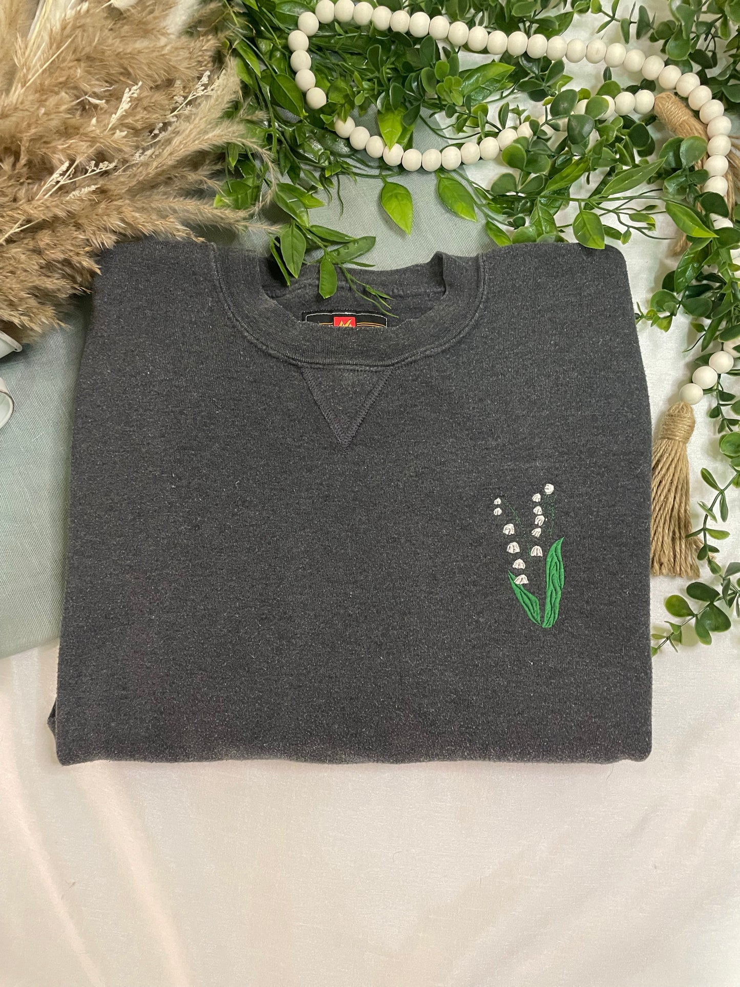 Dark gray sweatshirt with a floral design on a decorative background with greenery and beads.